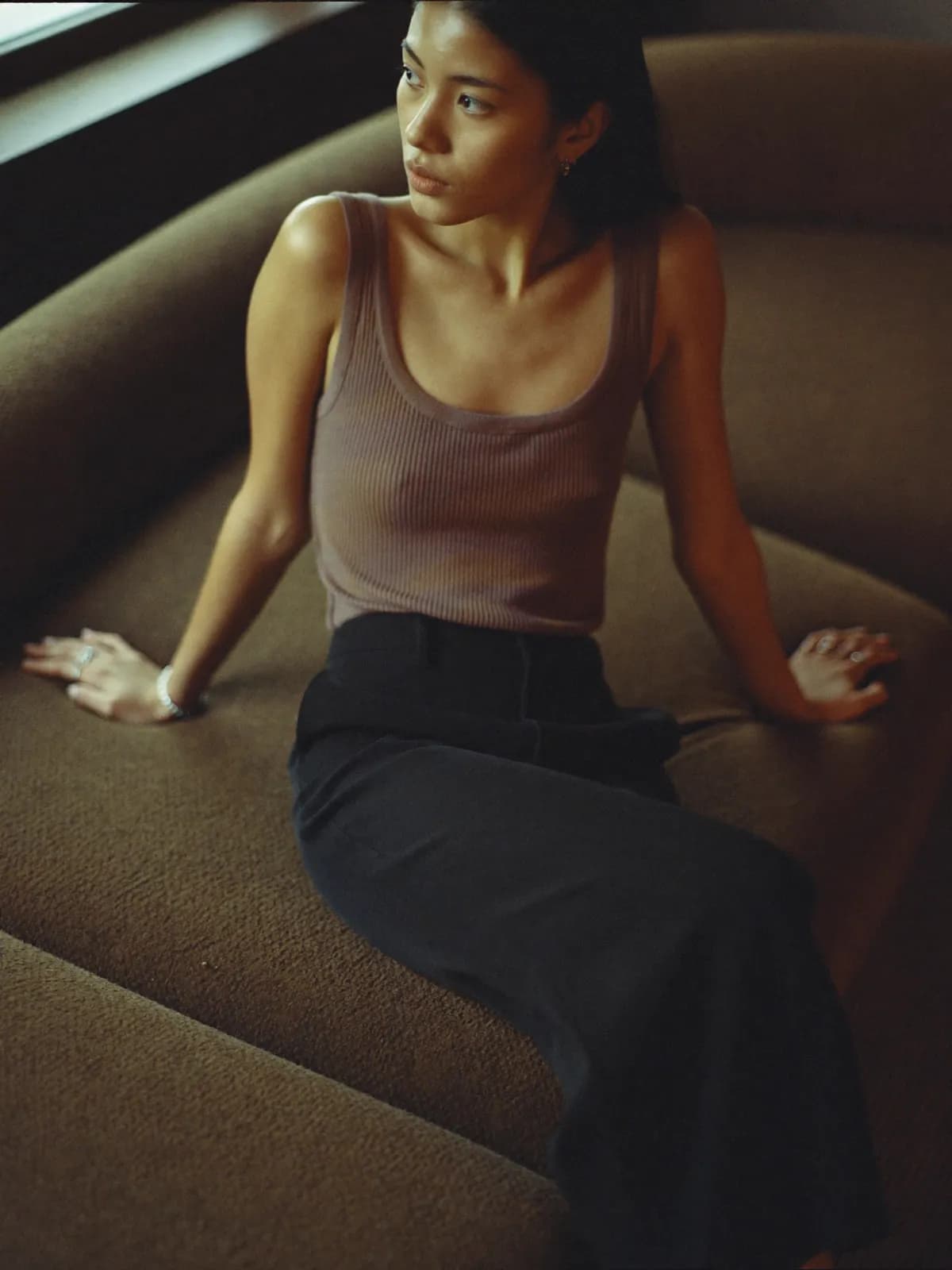 Woman in a taupe ribbed tank and black wide-leg trousers sitting on a brown sofa
